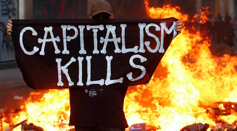 An anti-G20 protester stands in front of a burning street barricade and poses with a flag reading "Captitalism Kills" during with German riot police in Hamburg, Germany, July 7, 2017. REUTERS/Hannibal Hanschke